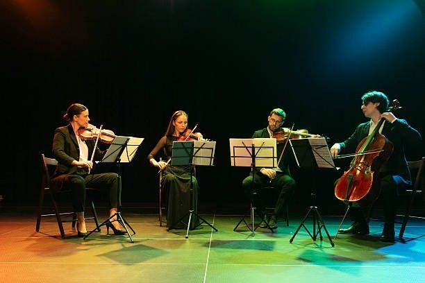 Four string musicians perform together on a dimly lit stage